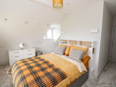 A bedroom with a bed with yellow and gray bedding a white dresser with a small mirror and a window at 21 The Rest in Porthcawl