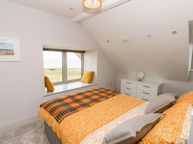 A bedroom with a bed covered in orange bedding a window seat with cushions and a white dresser at 21 The Rest in Porthcawl