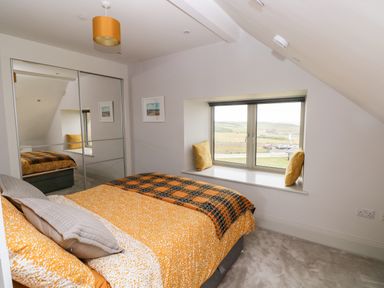 A bedroom with a bed covered in orange bedding a window seat with cushions and a mirrored wardrobe at 21 The Rest in Porthcawl