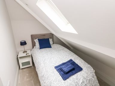 A small bedroom with a single bed with patterned bedding and blue pillow and towels beside a nightstand with a lamp at 21 The Rest in Porthcawl