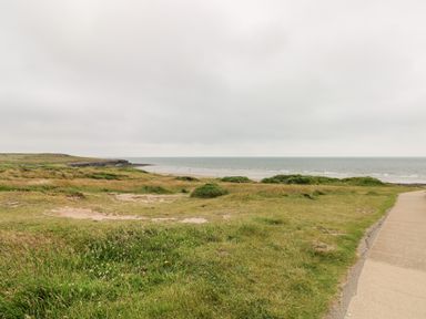 A grassy coastal landscape with a path leading to a sandy beach and ocean at 21 The Rest in Porthcawl