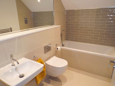 A bathroom with a wall-mounted sink and toilet next to a bathtub with a handheld shower at 21 The Rest in Porthcawl