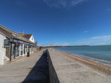 A seaside walkway with a fish and chips shop on the left and a beach with water on the right at Wrens Nest in Slapton