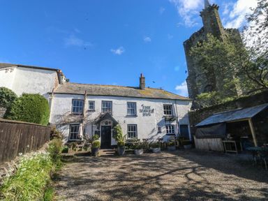 A white building with outdoor tables and potted plants next to a stone tower under a blue sky at Wrens Nest in Slapton