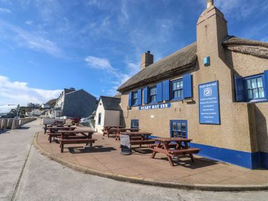The exterior of a pub with blue shutters and multiple wooden picnic tables on the pavement at Wrens Nest in Slapton