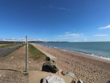 A beach with a road and people walking along the shore at Wrens Nest in Slapton