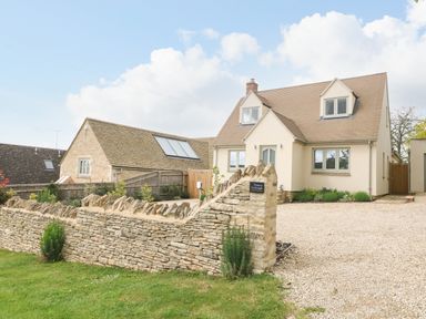 A stone wall in front of a two story house with a gravel driveway at Tawny Cottage Fulbrook near Burford