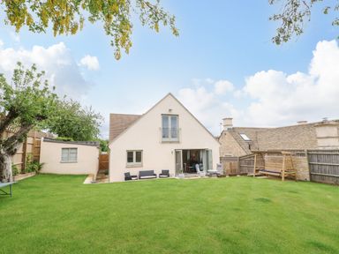 A backyard with green grass and outdoor seating in front of a cream house with a balcony at Tawny Cottage in Fulbrook near Burford