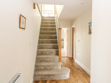 A carpeted staircase with wooden handrail in a hallway with wooden floor and open doors at Tawny Cottage in Fulbrook near Burford