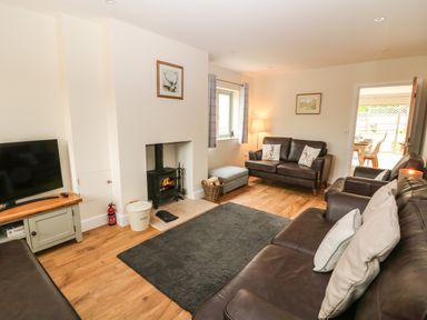 A living room with leather sofas a wood stove and a television at Tawny Cottage in Fulbrook near Burford