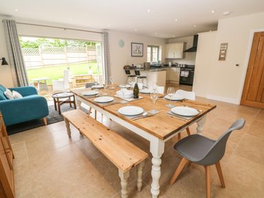 An open plan dining room and kitchen with a wooden dining table set for six and blue armchair at Tawny Cottage in Fulbrook near Burford