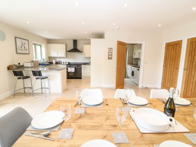 A dining table set with plates and glasses in an open kitchen and dining area with white cabinets and wooden doors at Tawny Cottage in Fulbrook near Burford