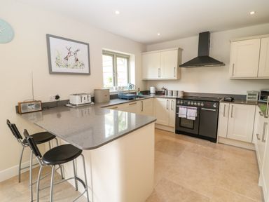 A kitchen with cream cabinets black stove gray countertop and two black bar stools at Tawny Cottage in Fulbrook near Burford