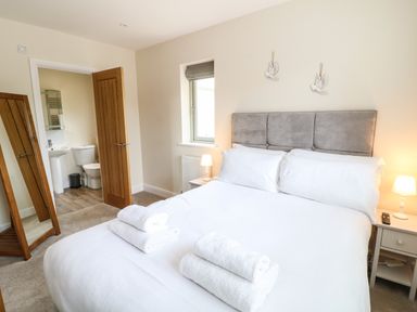 A bedroom with a bed white linens towels bedside tables lamps a window a mirror and an open door to a bathroom at Tawny Cottage in Fulbrook near Burford