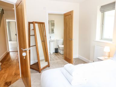 A bedroom with a bed with towels on it a standing mirror an open door showing a bathroom at Tawny Cottage in Fulbrook near Burford