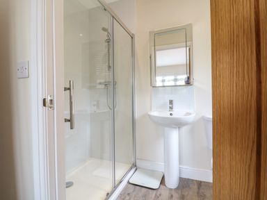 A bathroom with a glass shower enclosure a pedestal sink a mirror and a weighing scale on the floor at Tawny Cottage Fulbrook near Burford