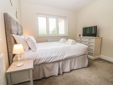 A bedroom with a bed table lamp window and a dresser with a television at Tawny Cottage in Fulbrook near Burford