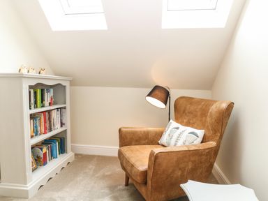 A reading corner with a leather armchair bookshelf and floor lamp at Tawny Cottage Fulbrook near Burford