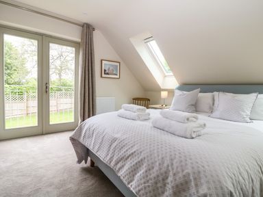 A bedroom with a bed with folded towels bedside table lamp wooden chair and glass doors leading outside at Tawny Cottage in Fulbrook near Burford
