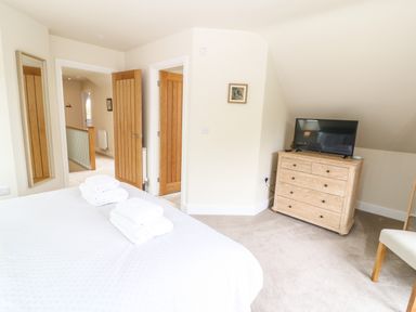 A bedroom with a bed with folded towels a wooden dresser with a television and a chair at Tawny Cottage in Fulbrook near Burford