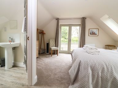 A bedroom with a bed and folded towels next to a door with curtains and an adjoining bathroom at Tawny Cottage in Fulbrook near Burford