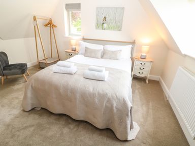 A bedroom with a double bed bedside tables lamps a chair and a wooden clothes rack at Tawny Cottage in Fulbrook near Burford