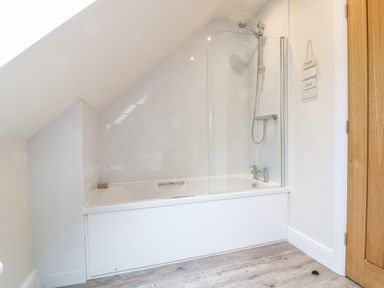 A bathroom with a bathtub shower combination under a slanted ceiling at Tawny Cottage Fulbrook near Burford