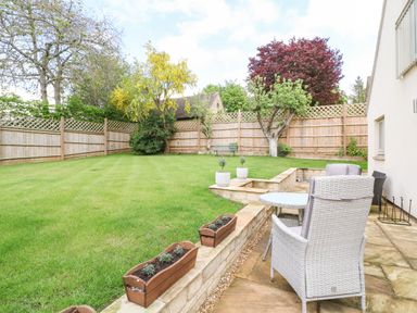 A garden with grass trees and wooden fence with outdoor chairs and table at Tawny Cottage in Fulbrook near Burford