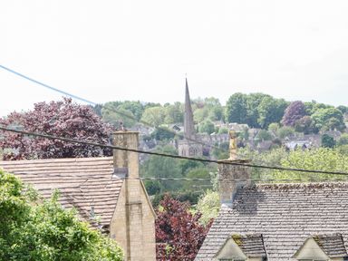 A view of rooftops and chimneys with trees and a church spire in the background at Tawny Cottage in Fulbrook near Burford