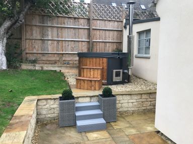 A garden area with a hot tub next to a house and stone steps with two plant pots at Tawny Cottage Fulbrook near Burford
