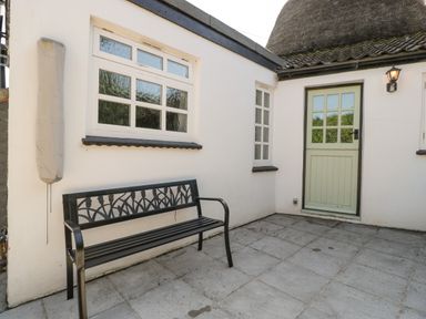 An outdoor patio with a metal bench next to a green door and two windows at 1 Old Thatch in Kilve