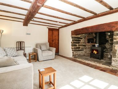 A sitting room with a stone fireplace and wooden ceiling beams at 1 Old Thatch in Kilve