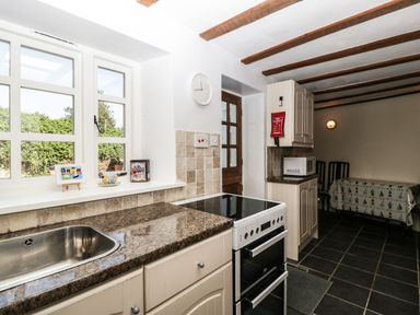A kitchen with a sink stove microwave and dining table at 1 Old Thatch in Kilve