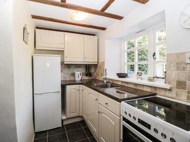 A kitchen with white cabinets a white refrigerator a stainless steel sink a stove and a window at 1 Old Thatch in Kilve