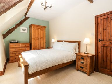 A bedroom with a wooden bed and nightstands with lamps wooden wardrobe and chest of drawers at 1 Old Thatch Kilve