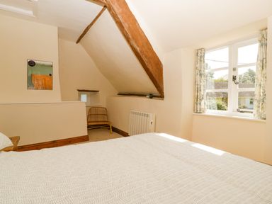 A bedroom with a bed under a window with floral curtains and wooden beams on the ceiling at 1 Old Thatch in Kilve