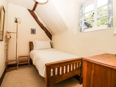 A bedroom with a single bed wooden furniture and a window with floral curtains at 1 Old Thatch in Kilve