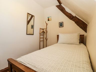 A small bedroom with a single bed wooden frame a mirror clothes rack and exposed wooden beams at 1 Old Thatch in Kilve