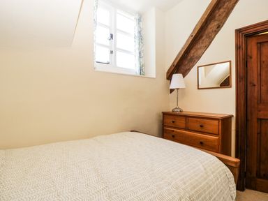 A bedroom with a bed next to a wooden dresser with a lamp and a mirror at 1 Old Thatch in Kilve