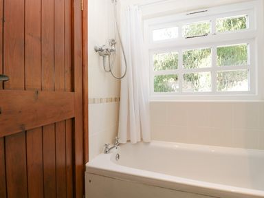 A bathroom with a bathtub shower curtain a wooden door and a window above the bathtub at 1 Old Thatch in Kilve