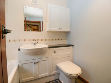 A bathroom with a sink, mirror, toilet, white cabinets, and tiled walls at 1 Old Thatch in Kilve