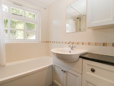 A bathroom with a bathtub a sink with cabinet a mirror and a frosted window at 1 Old Thatch in Kilve