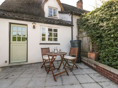 A small patio with wooden table and chairs outside a thatched cottage at 1 Old Thatch in Kilve