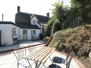 An outdoor patio area with a wooden table and metal chairs in front of a thatched cottage at 1 Old Thatch in Kilve