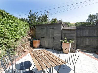 An outdoor patio with a wooden table and metal chairs next to a wooden garden shed and plants at 1 Old Thatch Kilve
