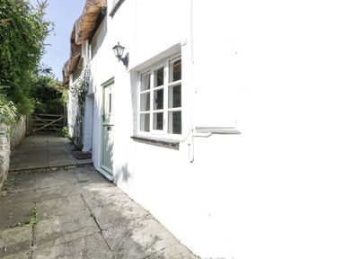 A pathway with stone tiles leading to a green door and window on a white building with a thatched roof at 1 Old Thatch in Kilve
