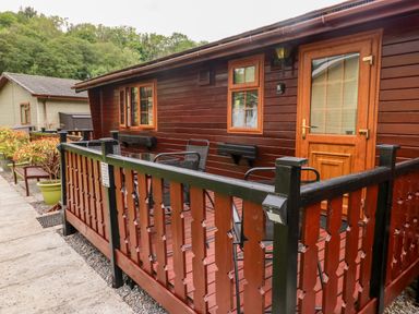 A wooden cabin with a porch featuring outdoor chairs and a table surrounded by a wooden railing at Heritage Park in Stepaside near Kilgetty