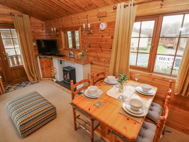 A wooden cabin interior with a dining table set for four near a window a television on a corner shelf and an ottoman at Heritage Park in Stepaside near Kilgetty