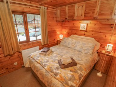 A bedroom with wooden walls a double bed with patterned bedding bedside tables and lamps at Heritage Park Stepaside near Kilgetty