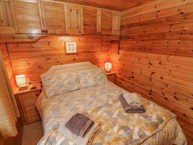A bedroom with a double bed two bedside tables with lamps wooden walls and cabinets at Heritage Park Stepaside near Kilgetty